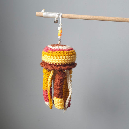 Warm orange and red crochet jellyfish dangling from wooden stick with a bell— interactive cat wand toy.